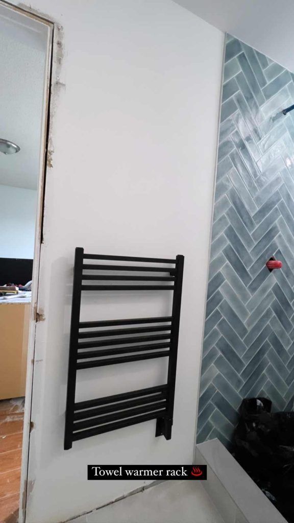 Black wall-mounted towel radiator beside a mirror, next to a tiled shower wall.