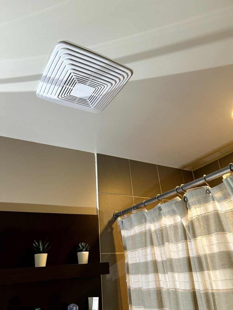 Ceiling-mounted square ventilation fan above a shower curtain in a bathroom