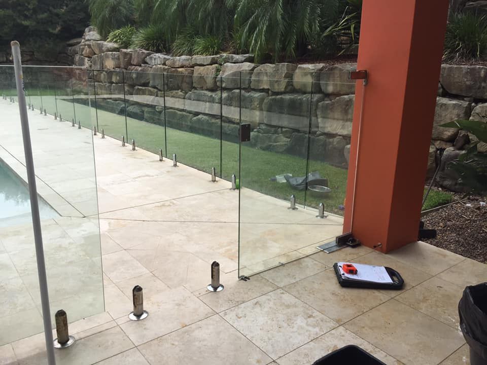 A Glass Fence Surrounds A Swimming Pool With A Brick Wall In The Background — Avoca Beach Glass In Gosford, NSW