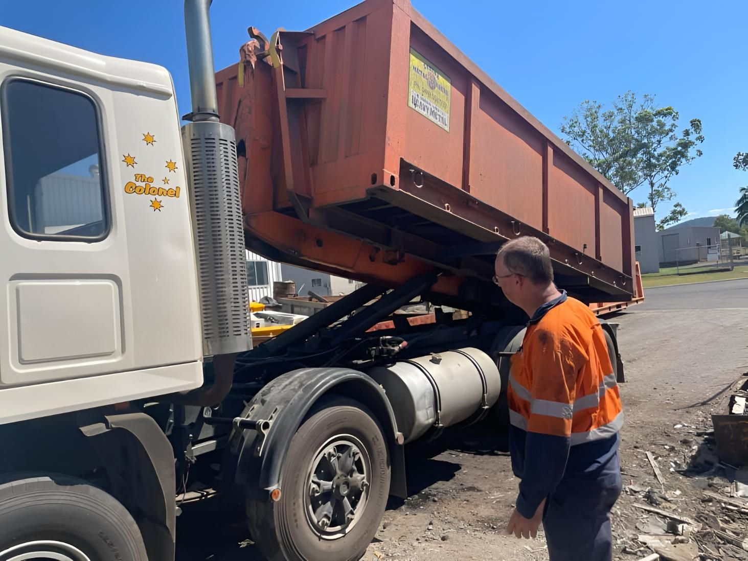 A Man In An Orange Vest Is Standing Next To A Dump Truck — Mackay Hose Fitting Services In West Mackay, QLD