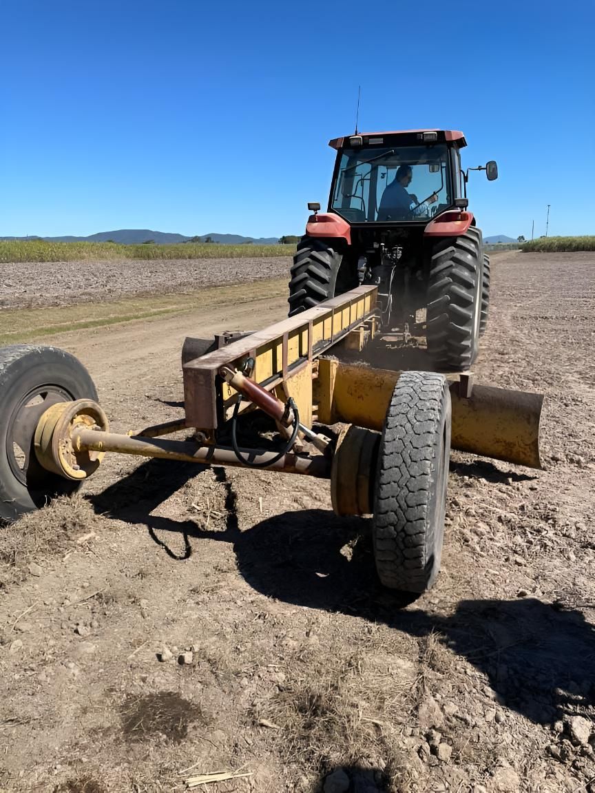A Tractor Is Driving Down A Dirt Road  With A Trailer Attached To It — Mackay Hose Fitting Services In West Mackay, QLD
