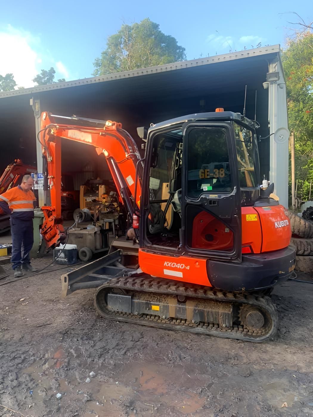 A Small Orange And Black Excavator Is Parked In Front Of A Building — Mackay Hose Fitting Services In West Mackay, QLD