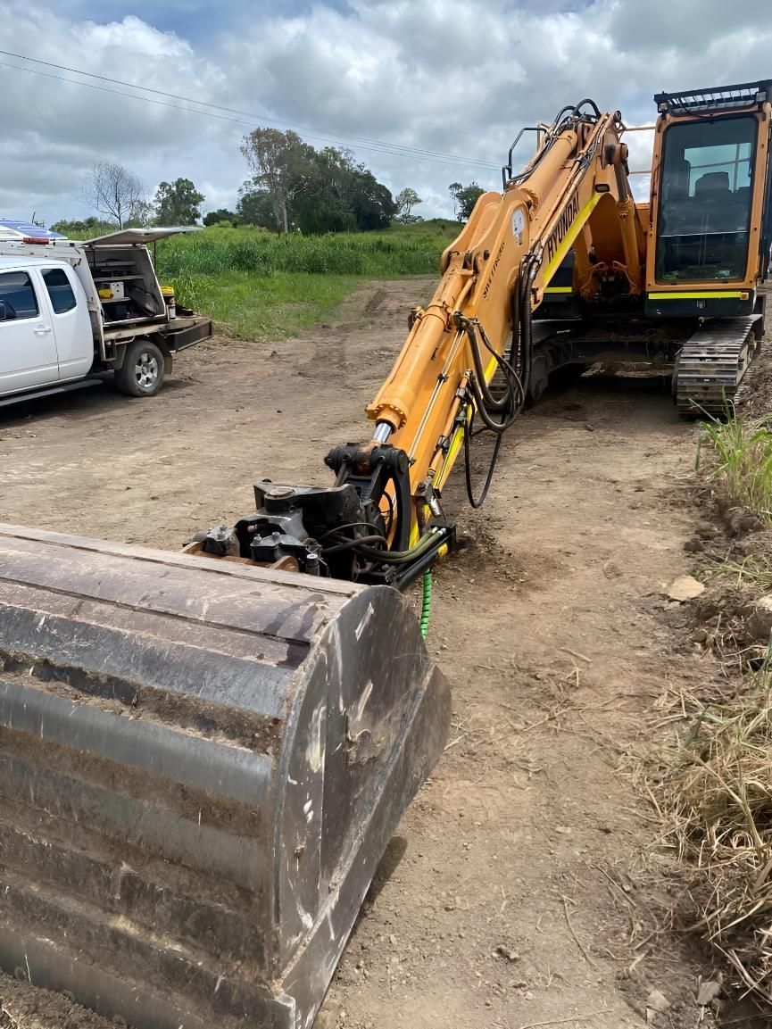 A Yellow Excavator Is Parked In A Dirt Field Next To A Truck — Mackay Hose Fitting Services In West Mackay, QLD