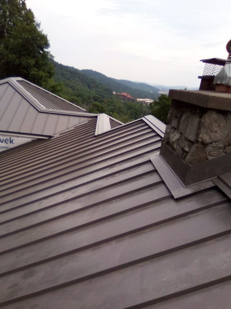 Metal roof with mountain view, angled lines, brown and gray hues, chimney, overcast sky.