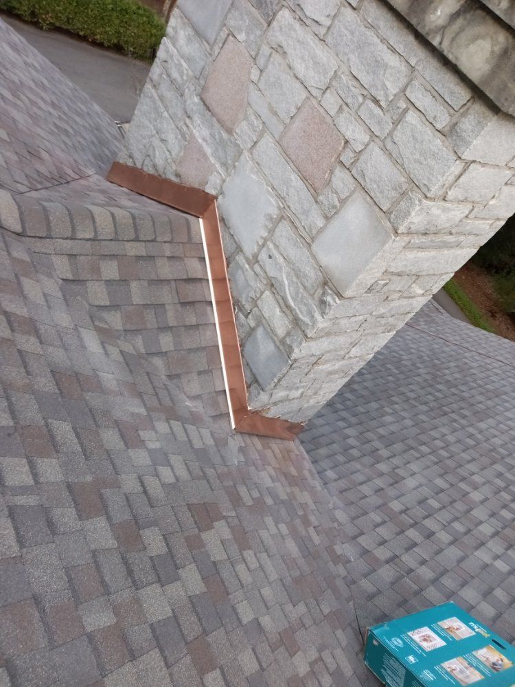 Copper flashing installed around a stone chimney on a shingled roof.