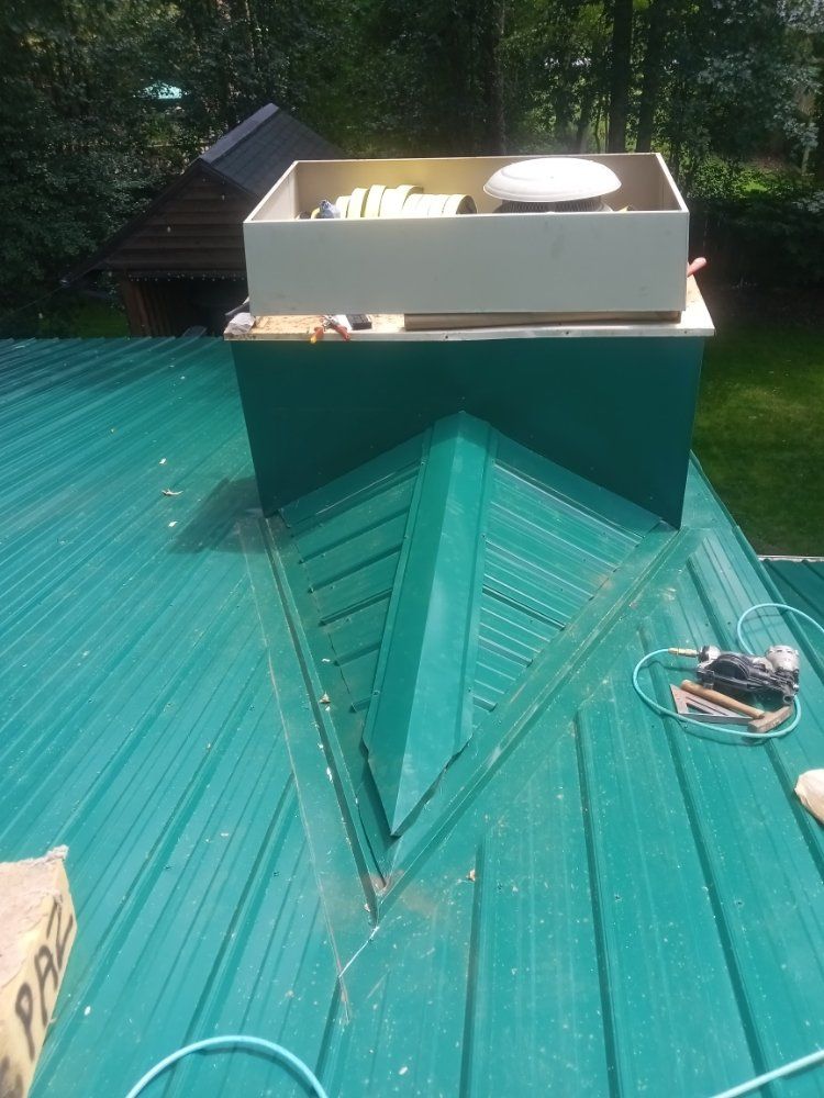 Green metal roof with chimney and equipment box on top; tools nearby.