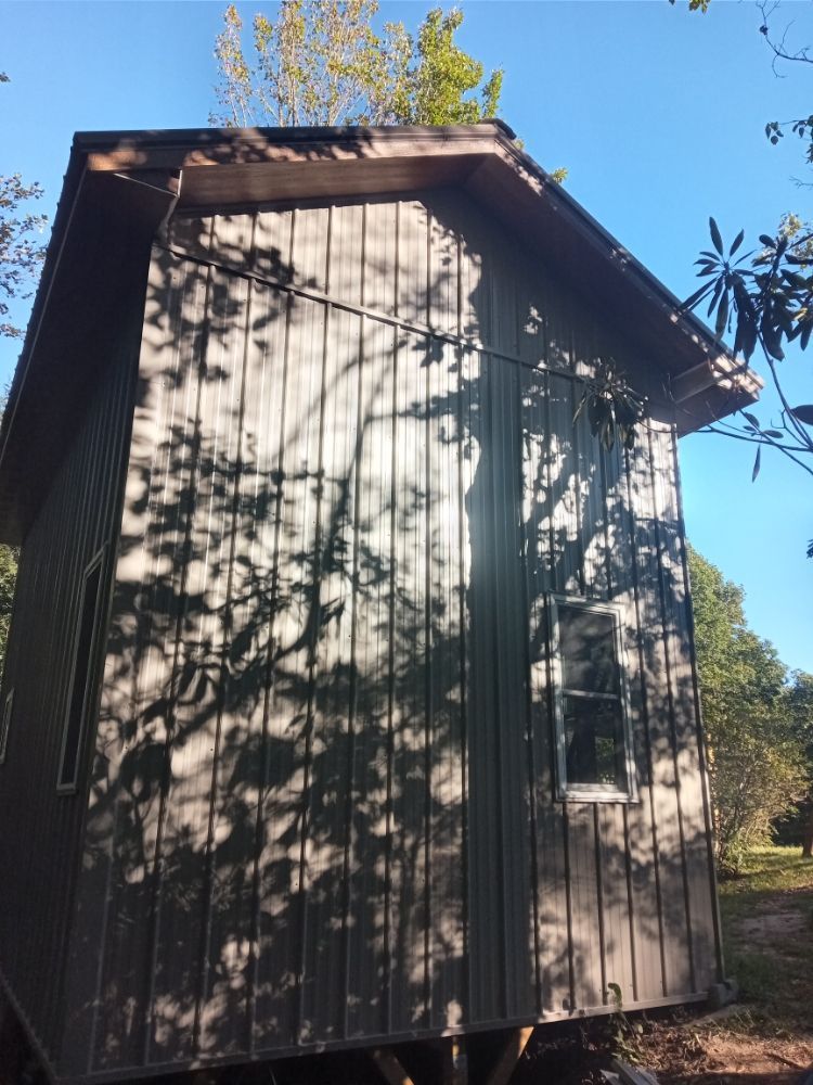 Wooden cabin with shadows from trees, under a blue sky.