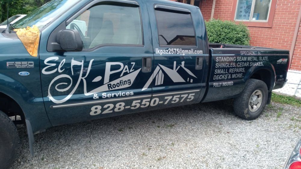 Dark blue El K-Paz Roofing truck parked on gravel. Contact info, logo visible on the side.