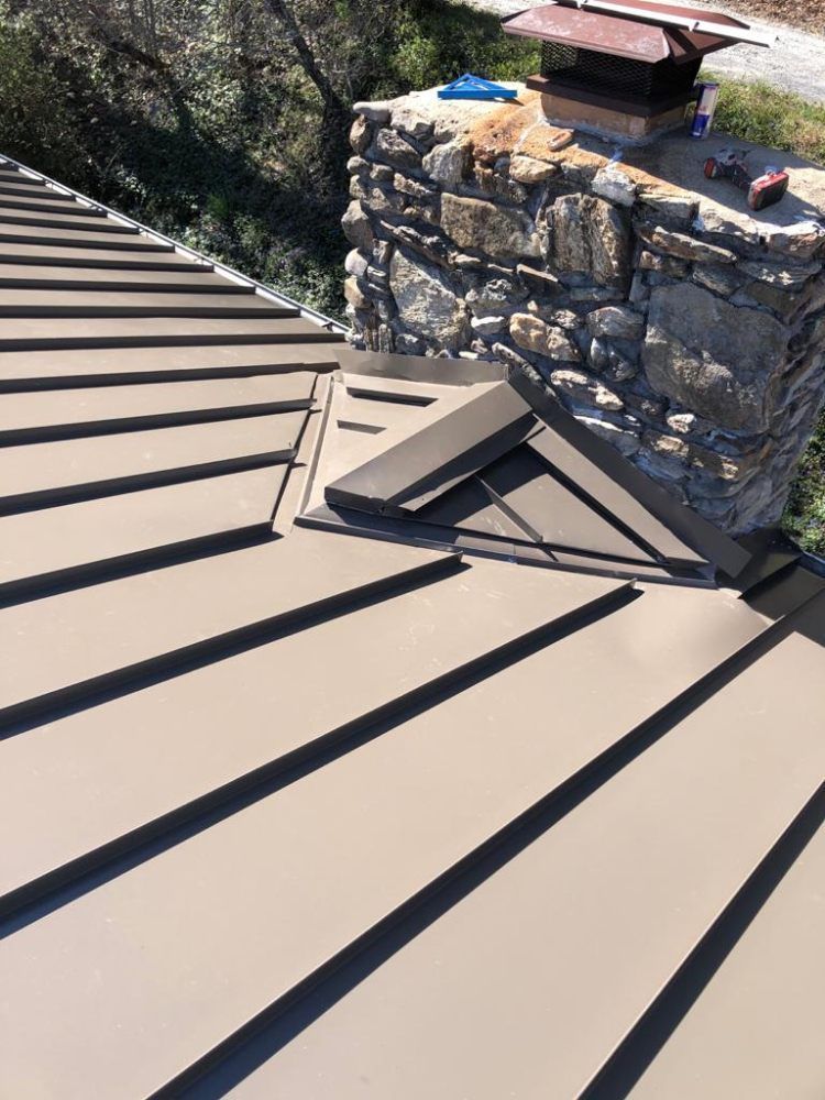 Brown metal roof with a stone chimney and a dark metal flashing.