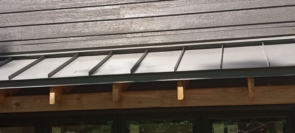 Close-up of a roof's edge, showing gray shingles above a metal and wood overhang.