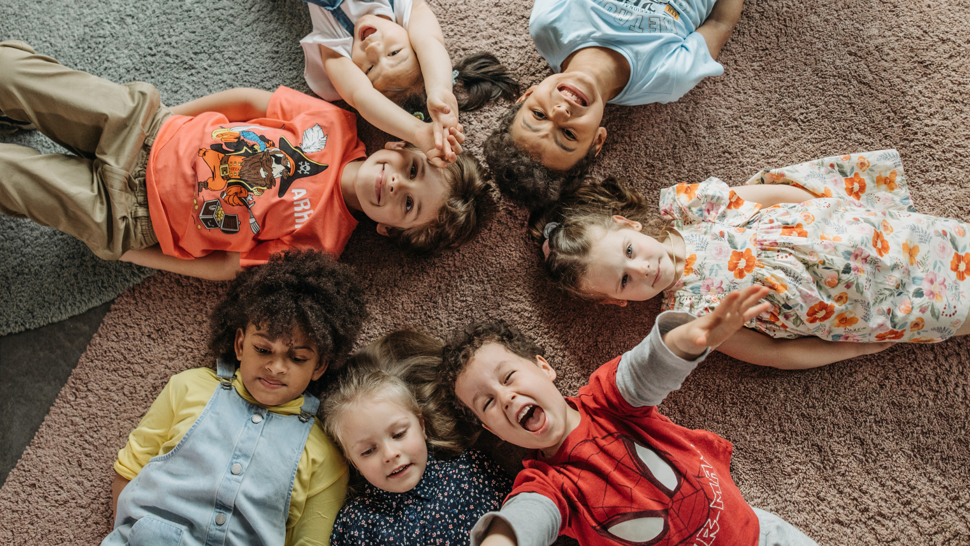 A group of children are laying on the floor in a circle.