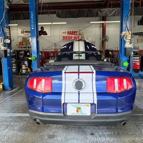 Blue Mustang convertible car in an auto shop, raised by a lift. White stripes and red taillights. | Premier Auto Service Center