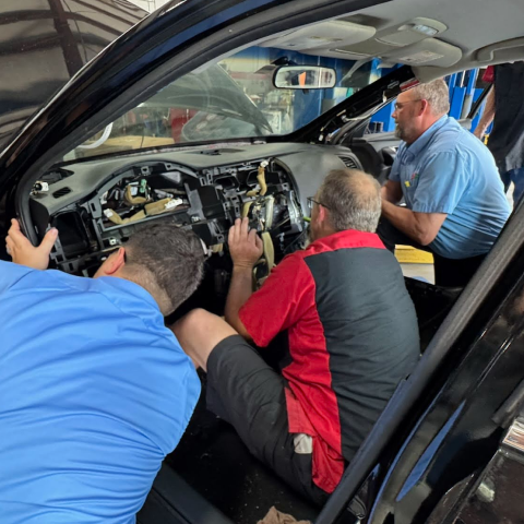 Three mechanics in a black car; removing the dashboard. One in blue, red-and-black, and light blue shirts work inside. | Premier Auto Service Center