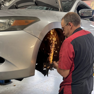 Mechanic using a grinder on a car's wheel well, producing sparks, in a shop. | Premier Auto Service Center