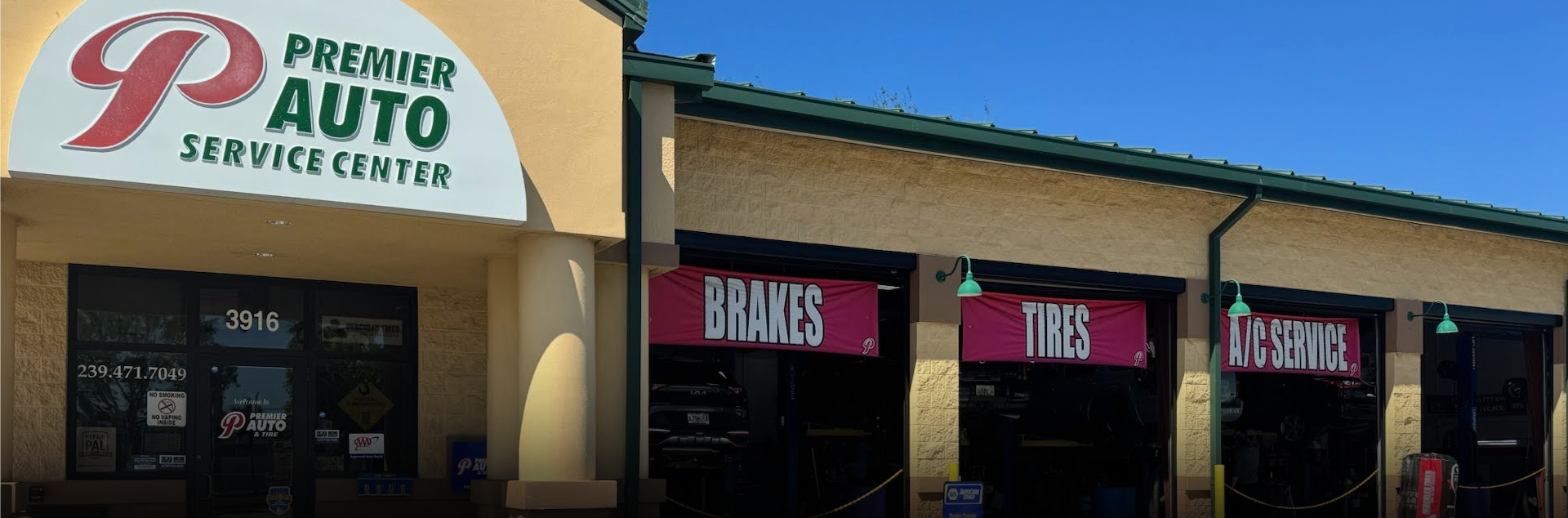 Exterior of an auto repair shop with open bays. Vehicles are inside for service, under bright sky. | Premier Auto Service Center