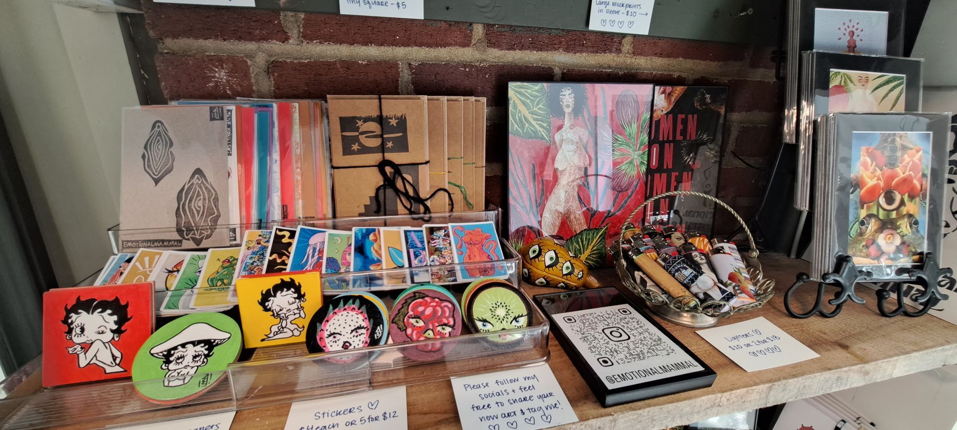 A display of Betty Boop art on a wooden shelf, including paintings and round coasters, with a brick wall background.
