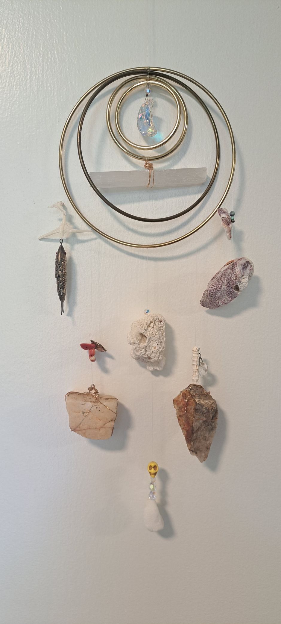 Dreamcatcher with various stones and beads hanging on a white wall.