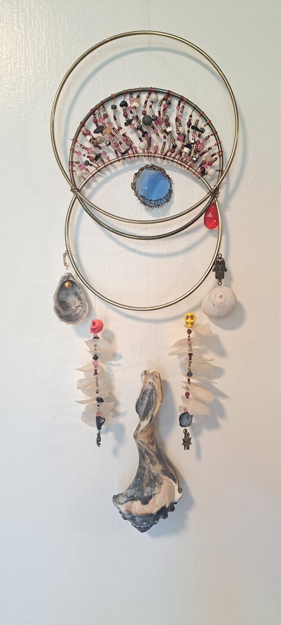 Dreamcatcher with beads and a shell-like figure against a white wall.