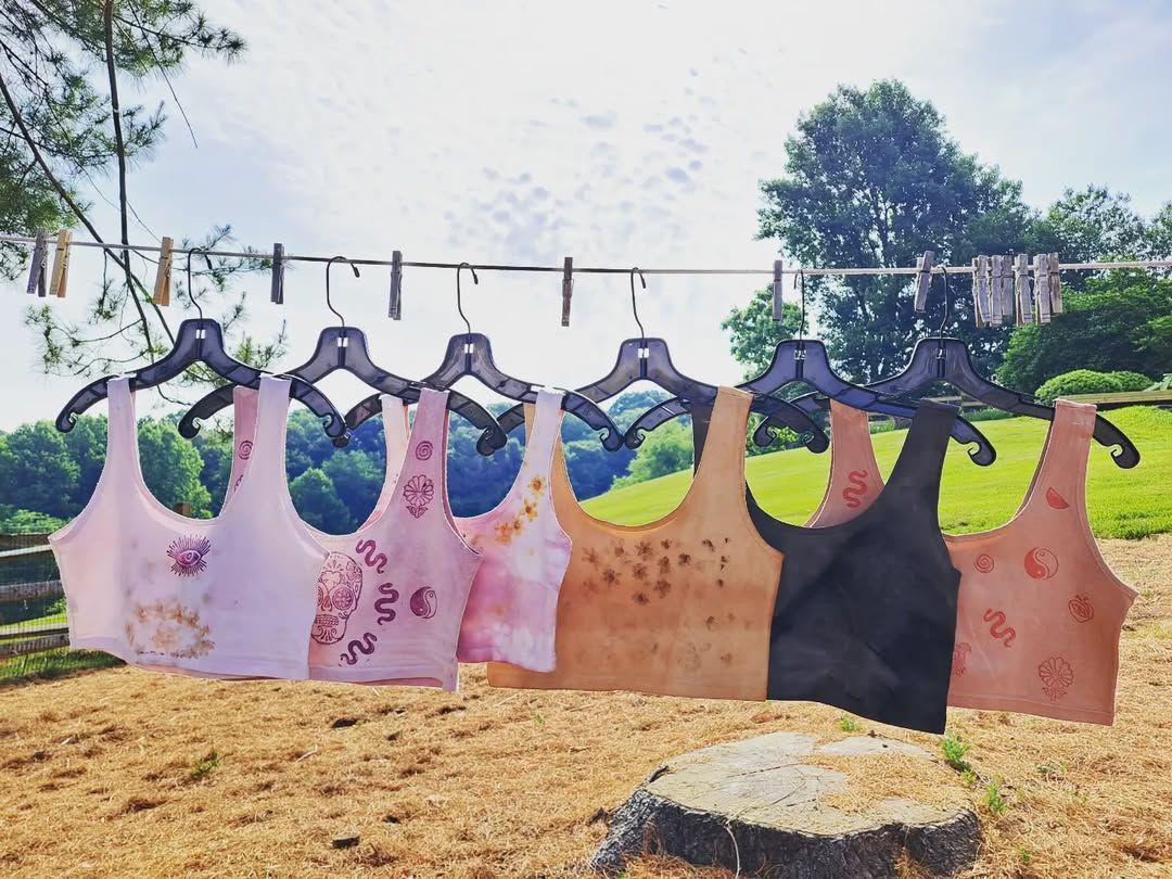Tank tops hanging on a clothesline outdoors, with a blurred forest and ground.