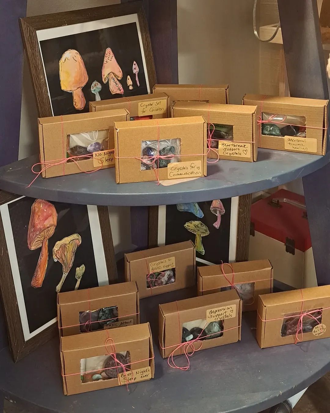 Display shelf with mushroom art and gift boxes. Brown boxes tied with string; framed mushroom art in the background.