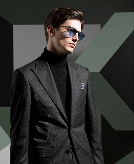 A man wearing a suit and sunglasses is standing in front of a geometric background.