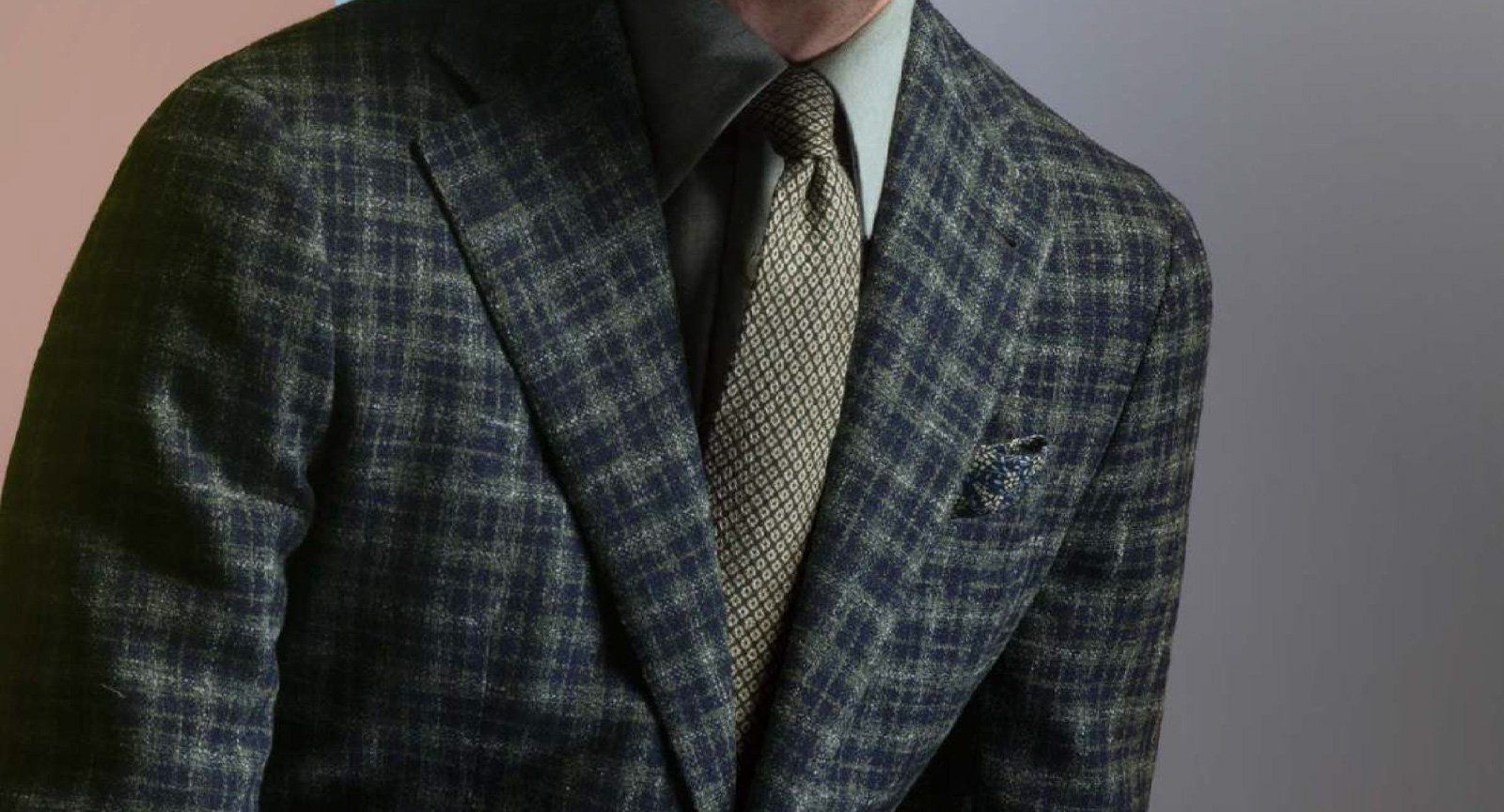 Man in patterned blue-green blazer, grey shirt, and patterned tie.