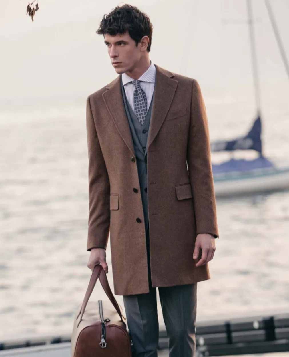 A man in a suit and tie is holding a brown duffel bag