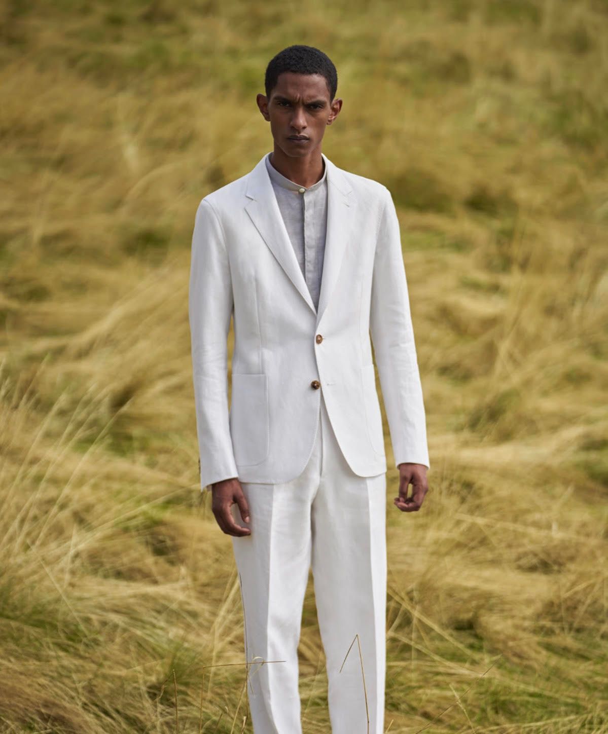 A man in a white suit is standing in a field of tall grass.