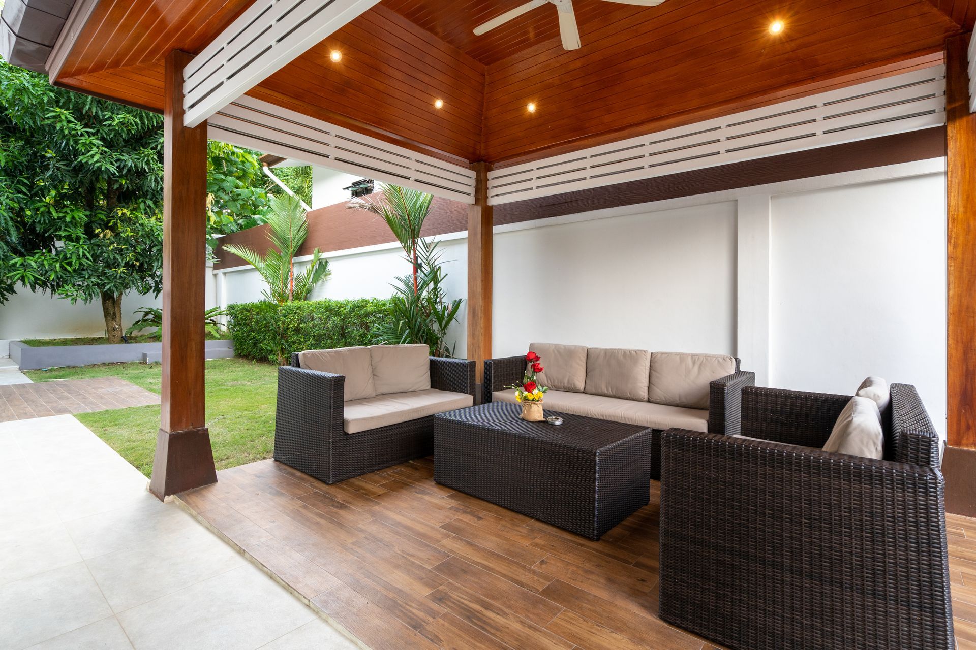 Covered outdoor patio with wicker furniture, wooden ceiling, and garden view.
