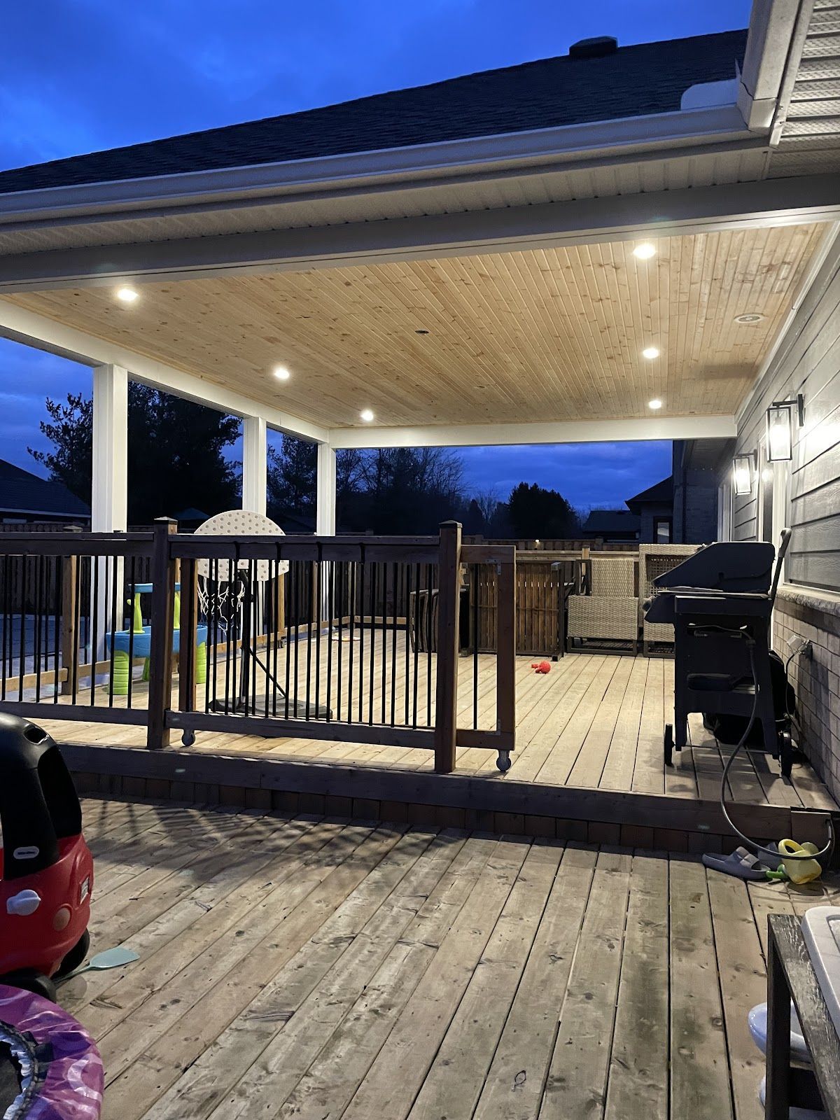 A wooden deck with a grill and a fence in front of a house at night.