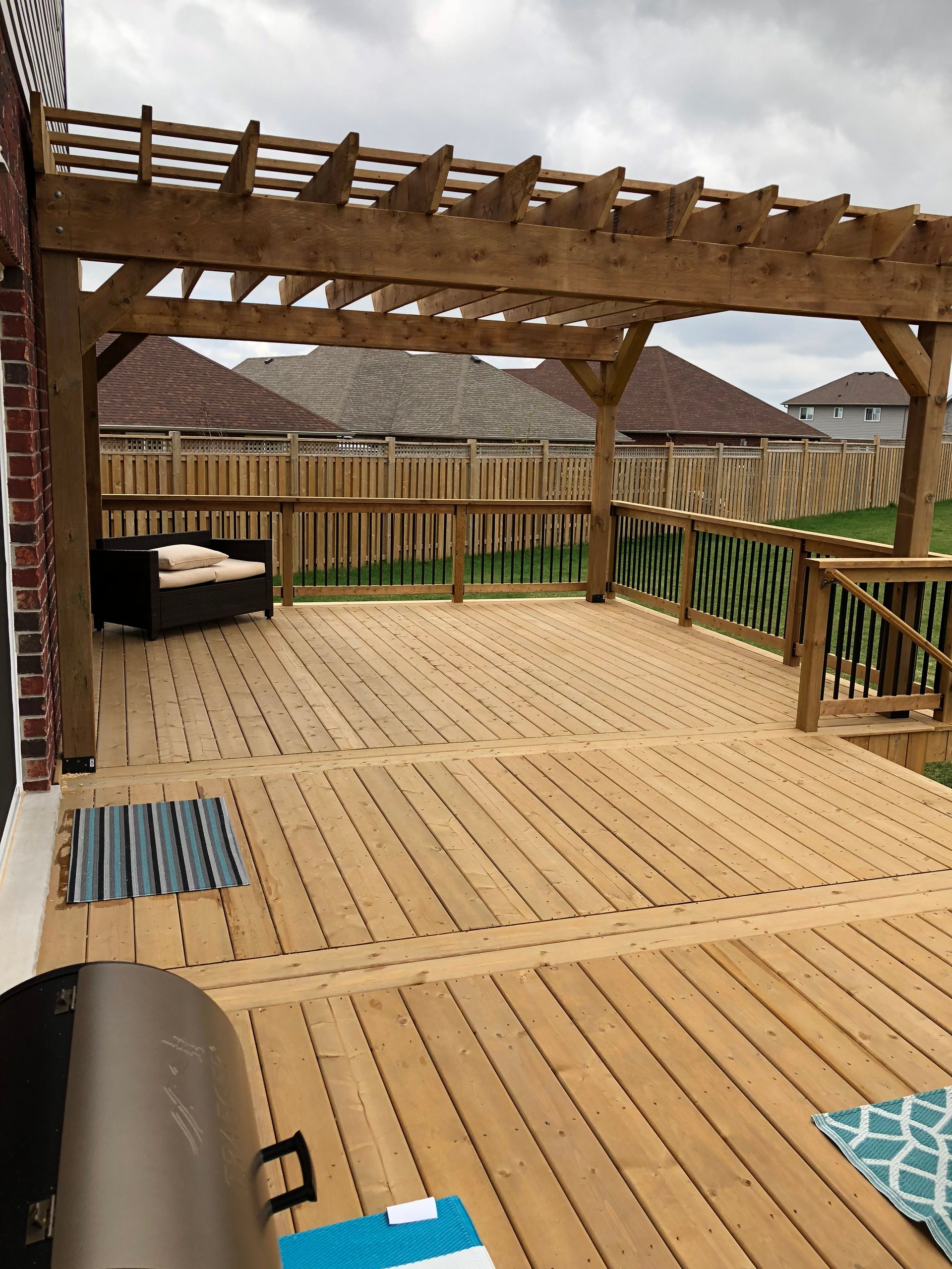 Wooden deck with pergola, furniture, and grill in a backyard.