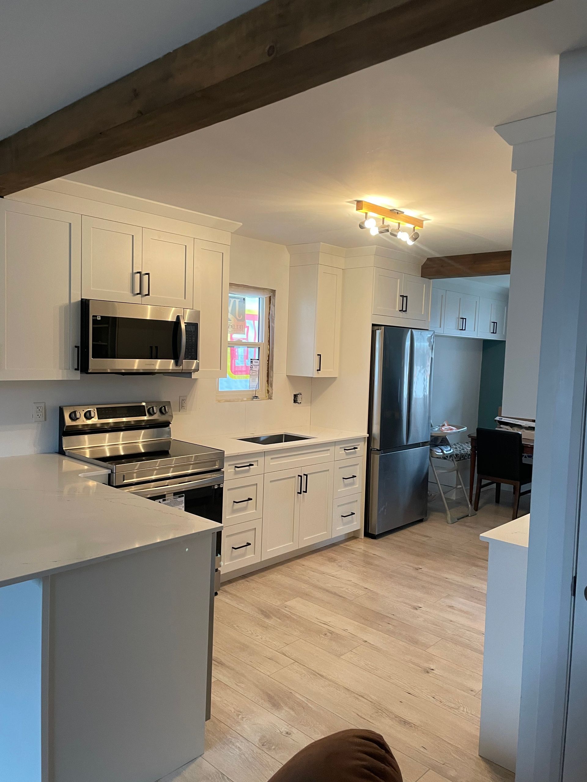 Modern white kitchen with stainless steel appliances, light wood floors, and a decorative wood beam.