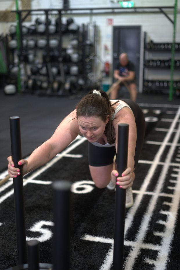 A woman is pushing a sled in a gym.