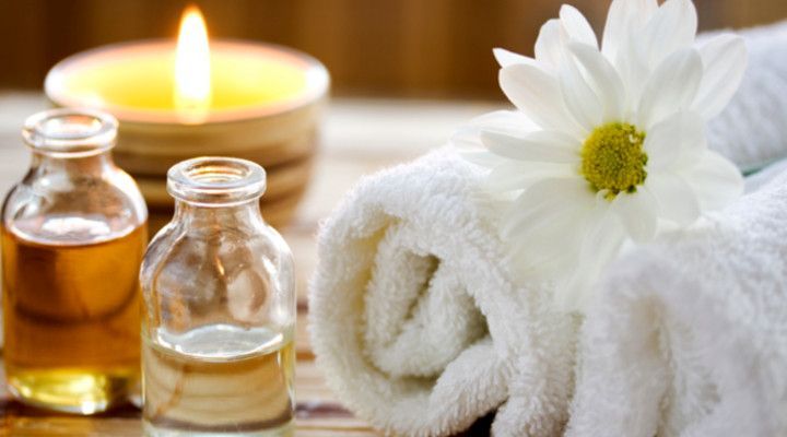 Sobre una mesa hay una vela, toallas, botellas de aceite y una flor.