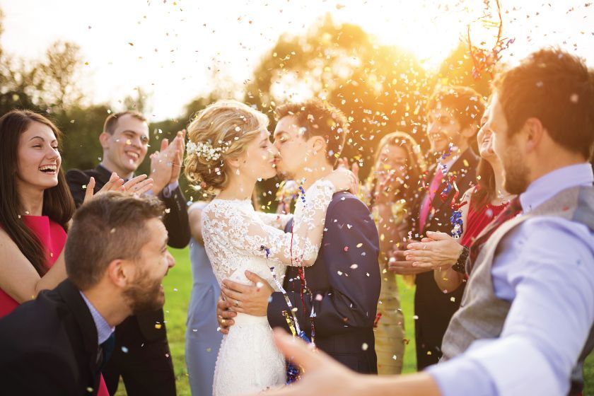 A bride and groom are kissing while their wedding guests throw confetti at them.