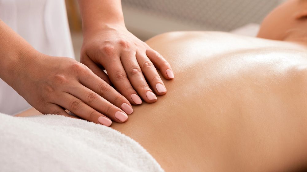 Mani che massaggiano il viso di una persona. Occhi chiusi. Sfondo blu e bianco.