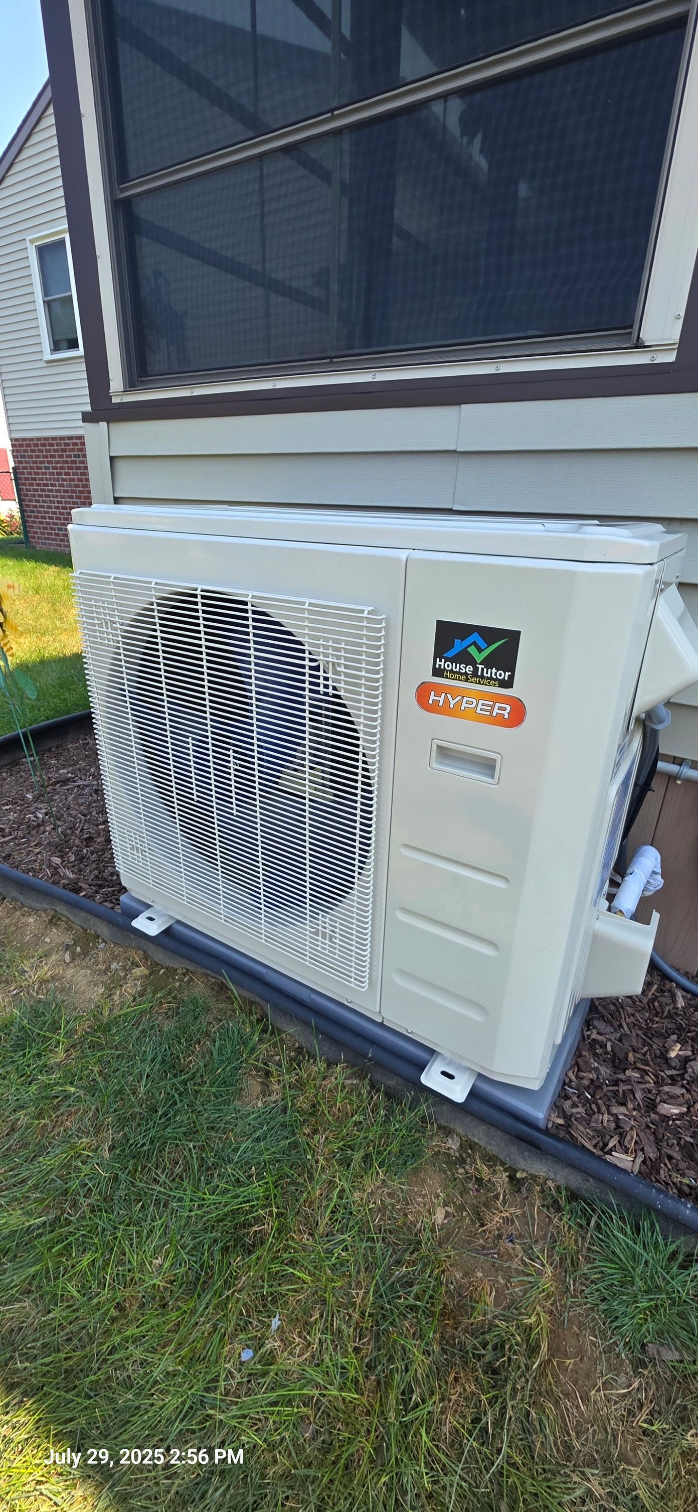 Mini-split heat pump unit installed outdoors next to a house with a screen window.