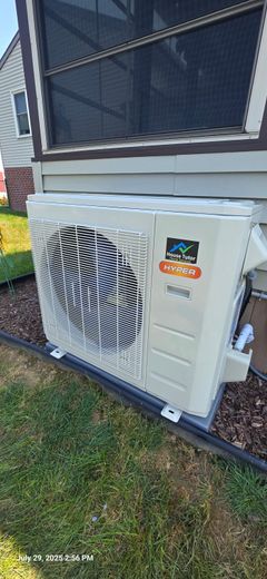 Mini-split heat pump unit installed outdoors next to a house with a screen window.