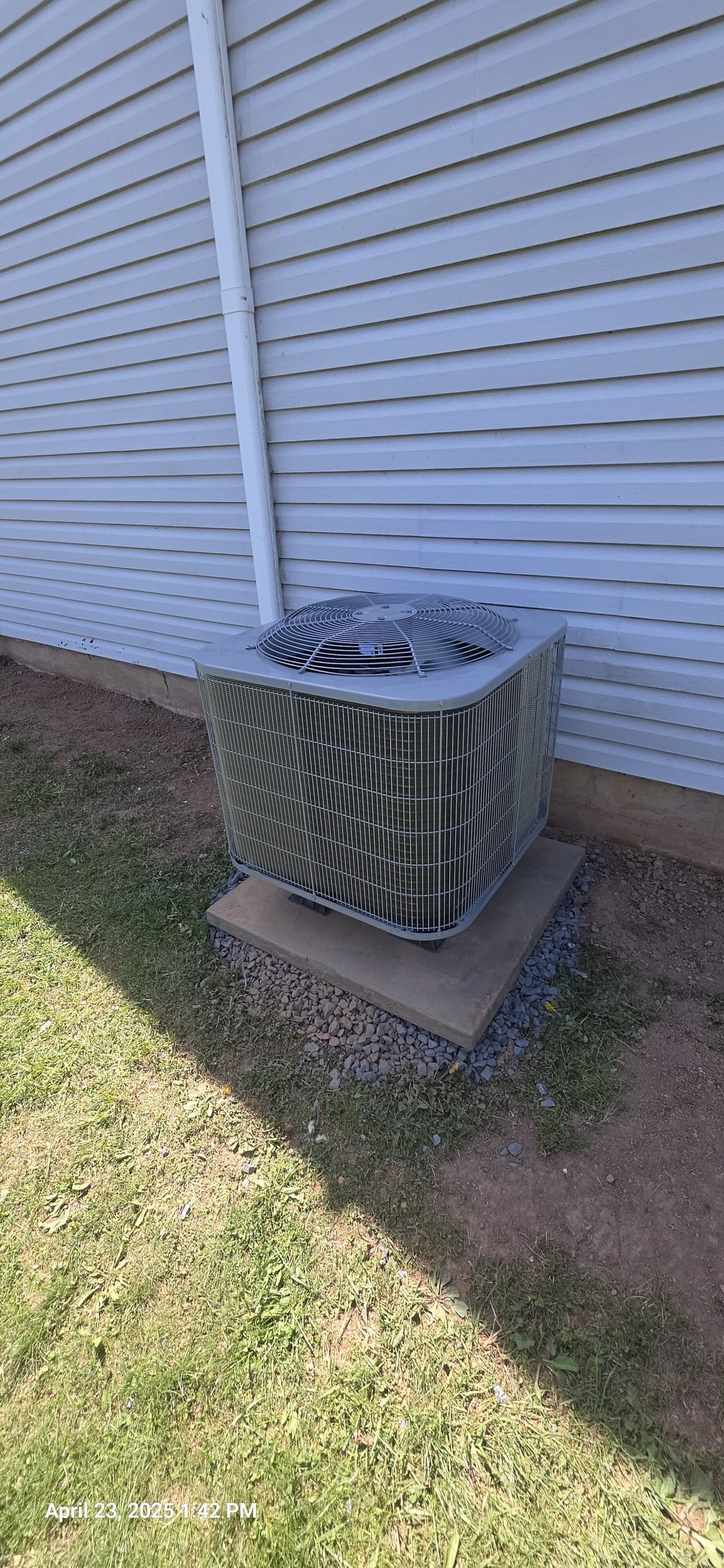 An air conditioning unit sits on a concrete pad next to a house with white siding.