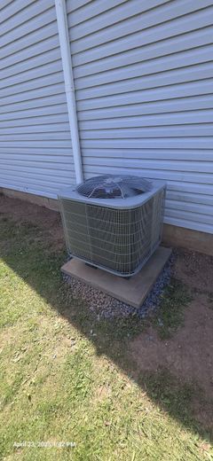 An air conditioning unit sits on a concrete pad next to a house with white siding.