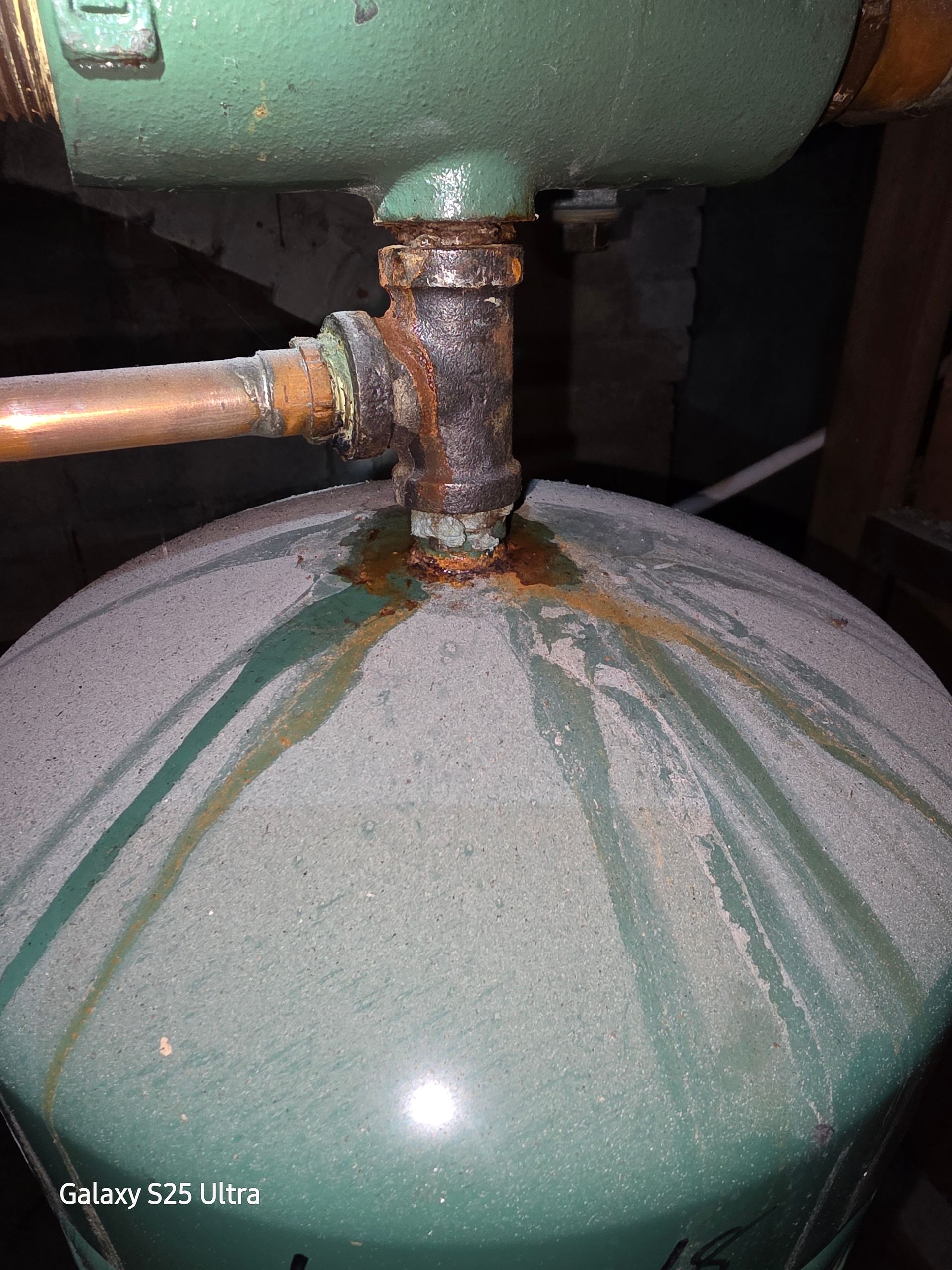 Corroded pipe fittings on a green tank with rust stains.