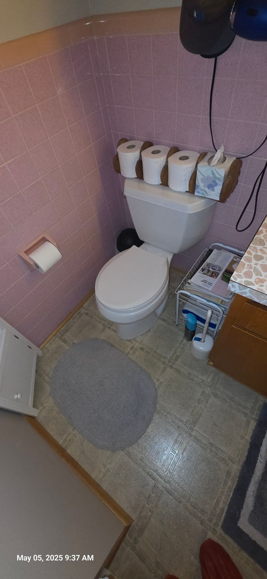 A bathroom with a toilet. Rolls of toilet paper and tissues sit on top of the tank.  Pink walls.