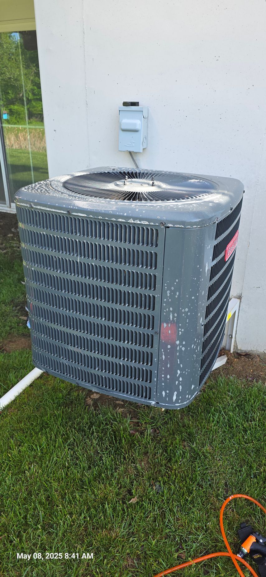 Air conditioning unit outside on grass near a white wall.