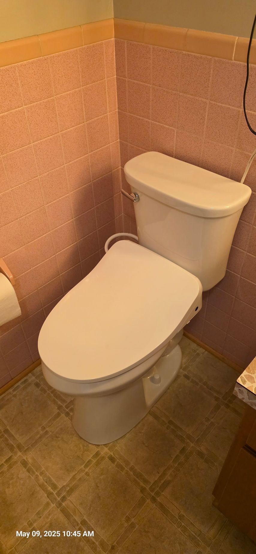Toilet with a white seat and tank in a bathroom with pink tiled walls.