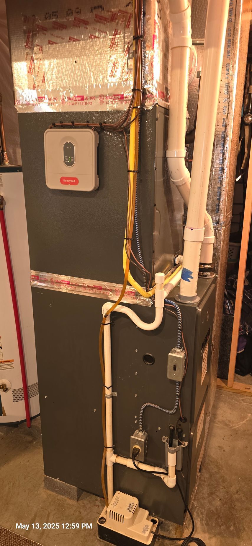 Furnace and related components in a basement setting. White PVC pipes and wiring are present.