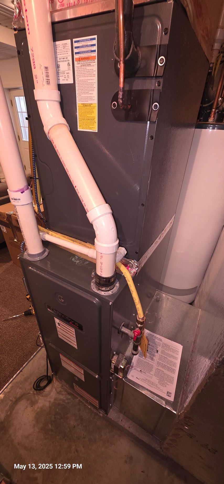 Furnace with white PVC pipes and yellow gas line. In a utility room.
