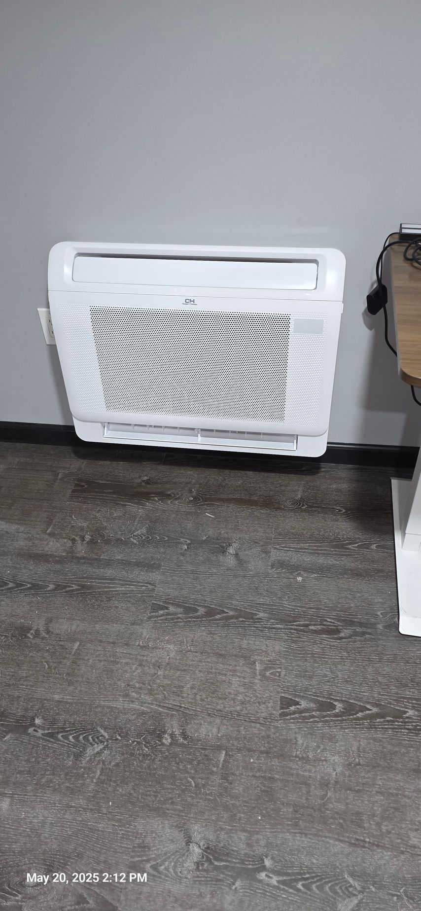 White air conditioner unit mounted on a gray wall. Dark gray floor in the foreground.