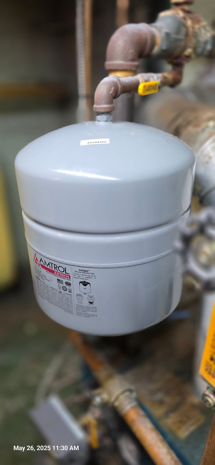 A gray expansion tank for a heating system connected to copper pipes.