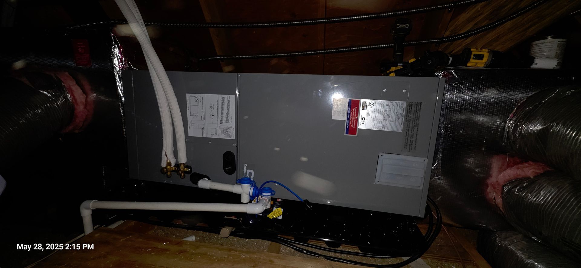 HVAC unit in an attic with white pipes and black ductwork.