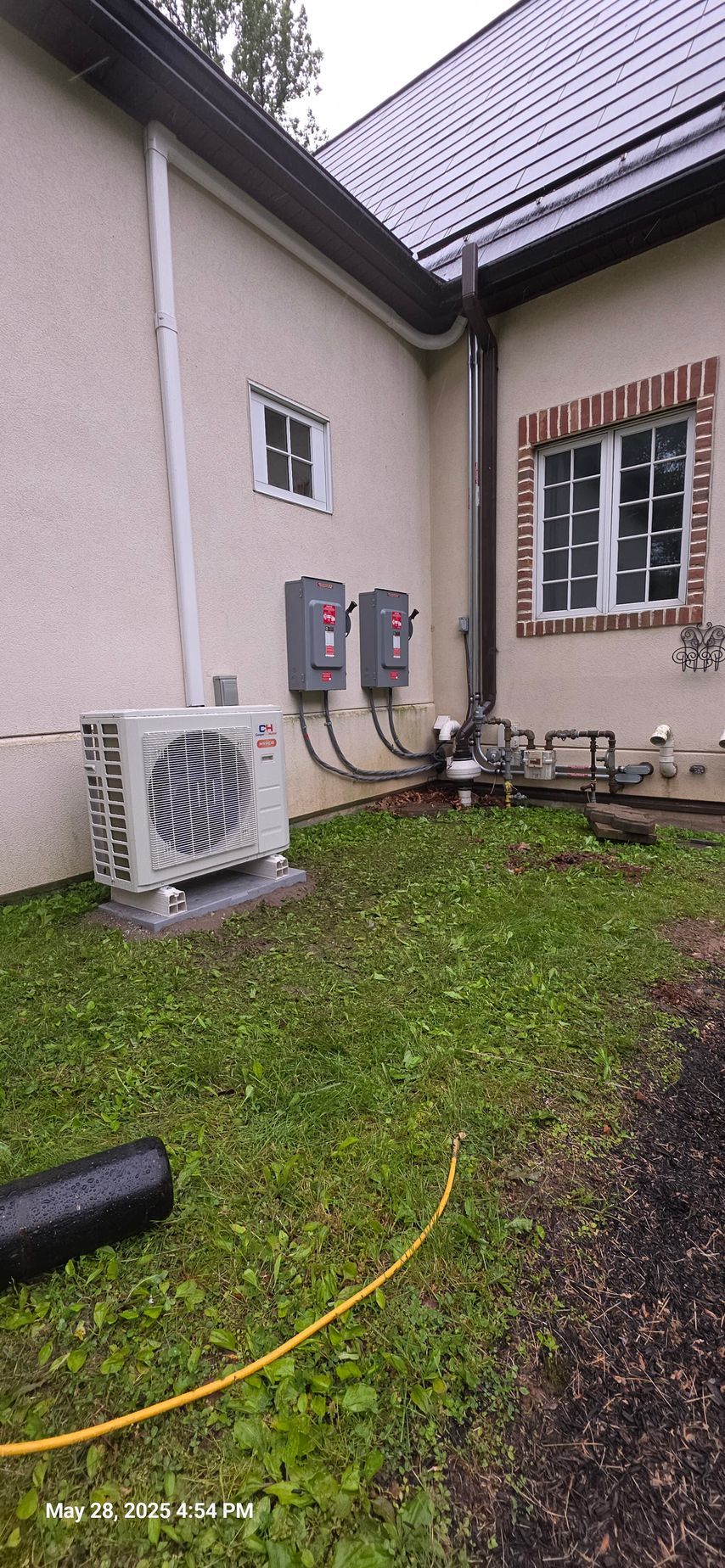 An air conditioning unit outside a stucco building, with electrical boxes and green grass.